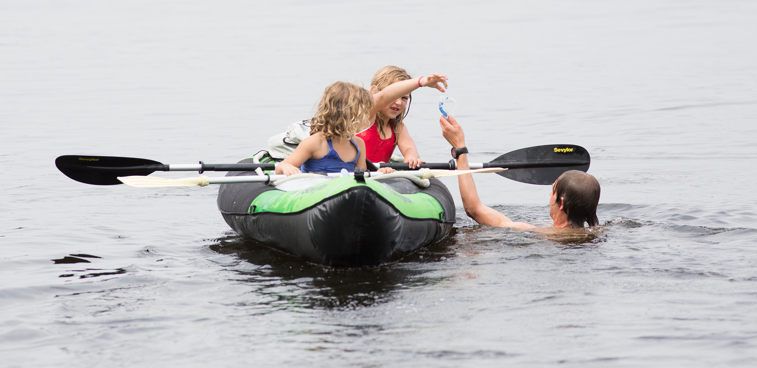 Kano op het water met 2 kinderen erin en 1 kind zwemt er naast.