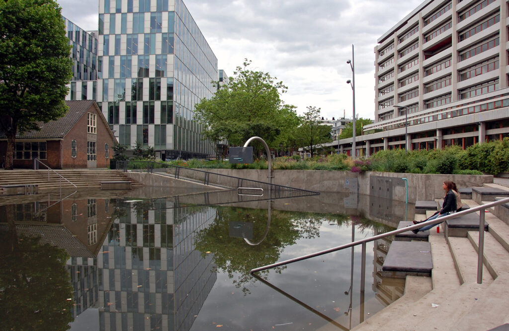 Met water gevuld waterplein in Rotterdam. Plein ligt tussen hoge panden op de rand zitten 2 tieners