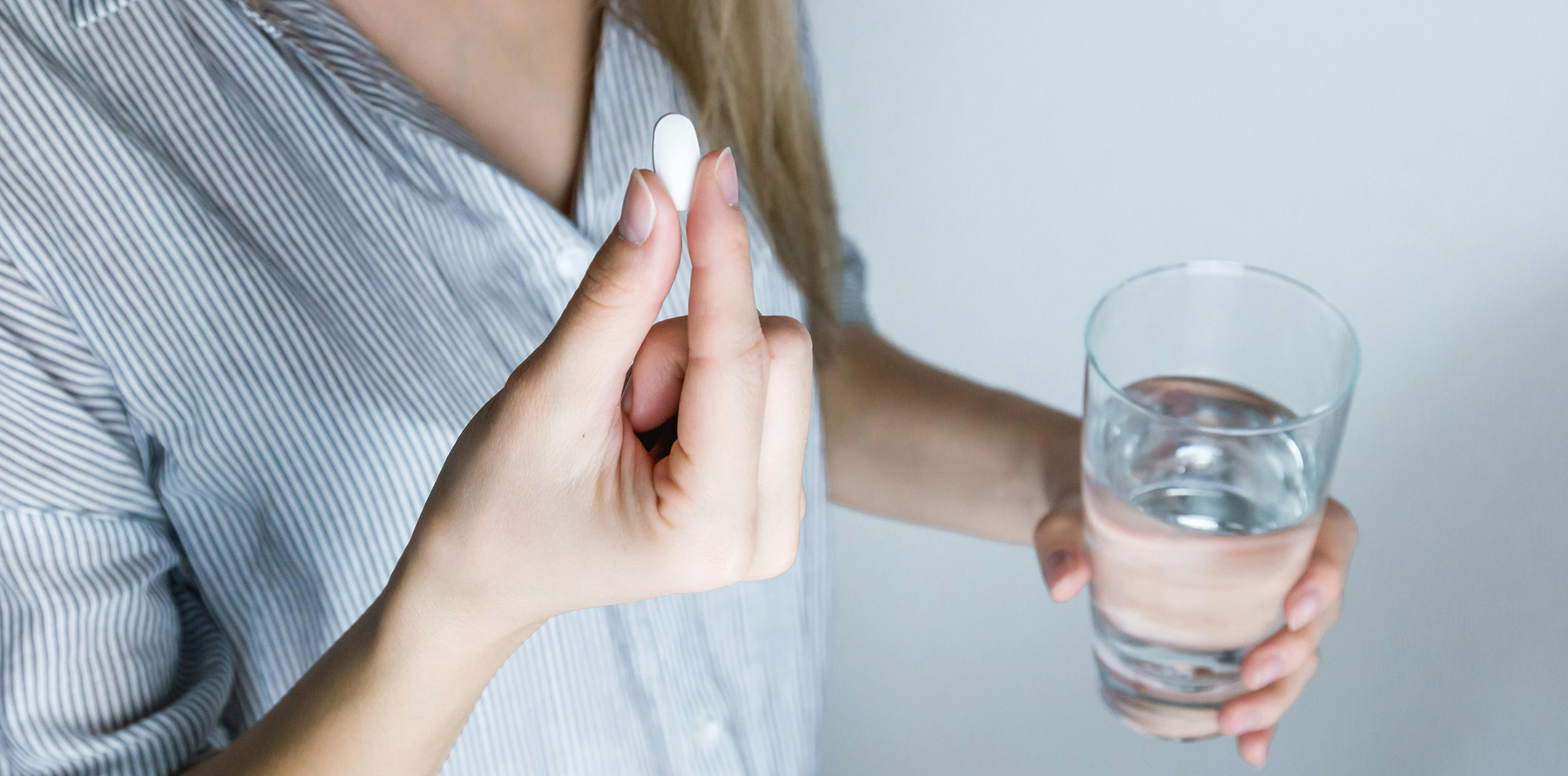 Vrouwelijke handen. In een hand een witte pil en de andere hand een glas water.