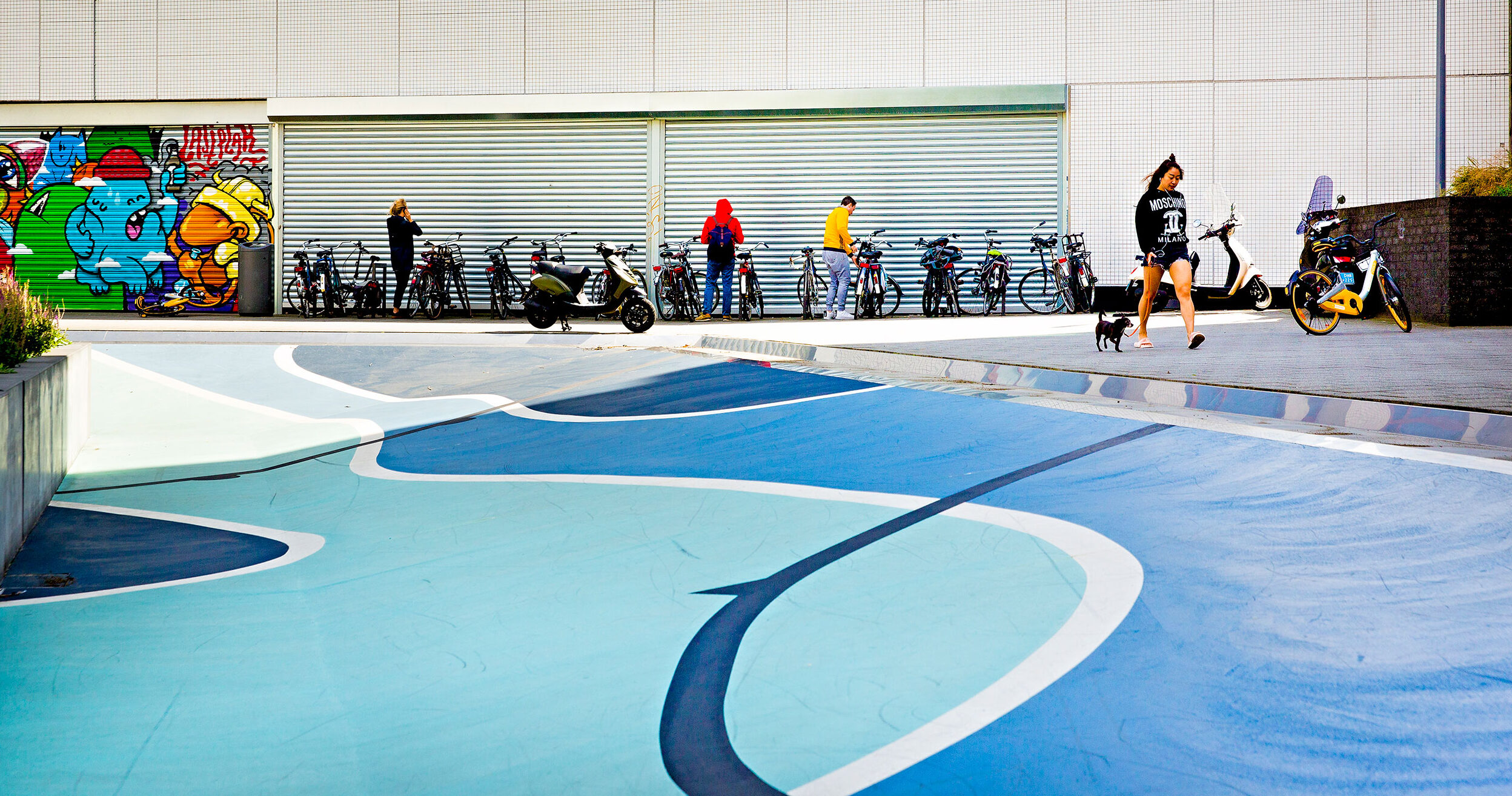 Betonnen bak met blauwe beschildering. er langs lopen jongeren.