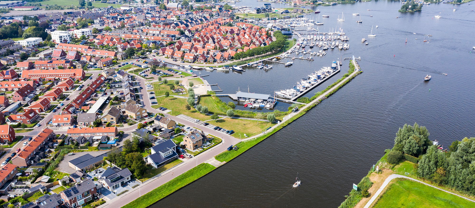 Luchtfoto: stad aan een groot water. De stad heeft o.a. een haven. Op het water varen o.a. zeilboten