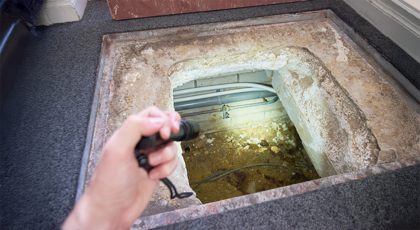 Droge kruipruimte waar vanuit de gang met een zaklamp in wordt geschenen.