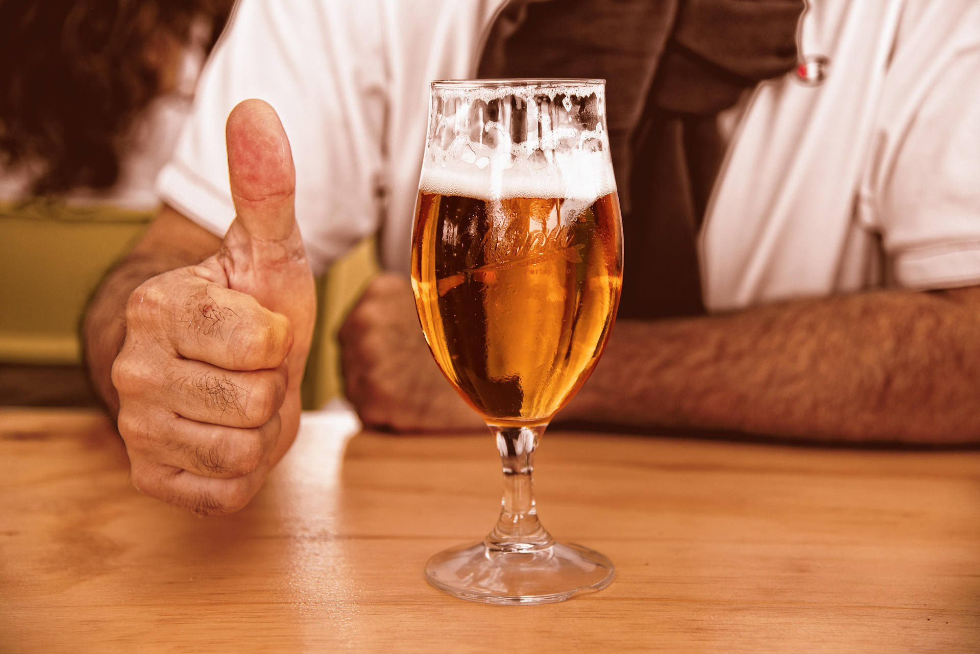 Glas bier op tafel met erachter een man die zijn duim opsteekt
