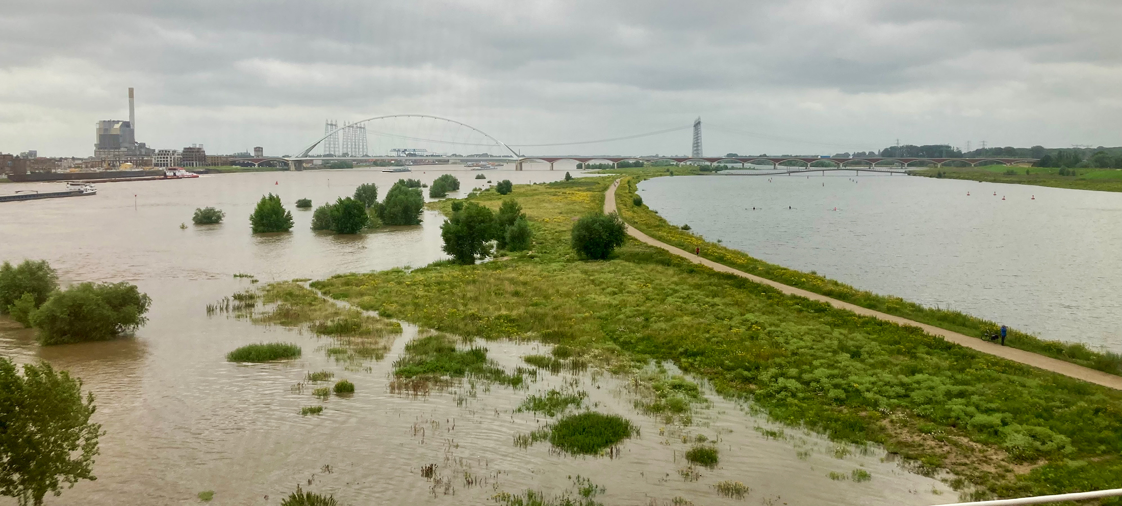 Hoog water in de IJssel. Onder gelopen uiterwaarden, brede rivier en de lucht is grijs.
